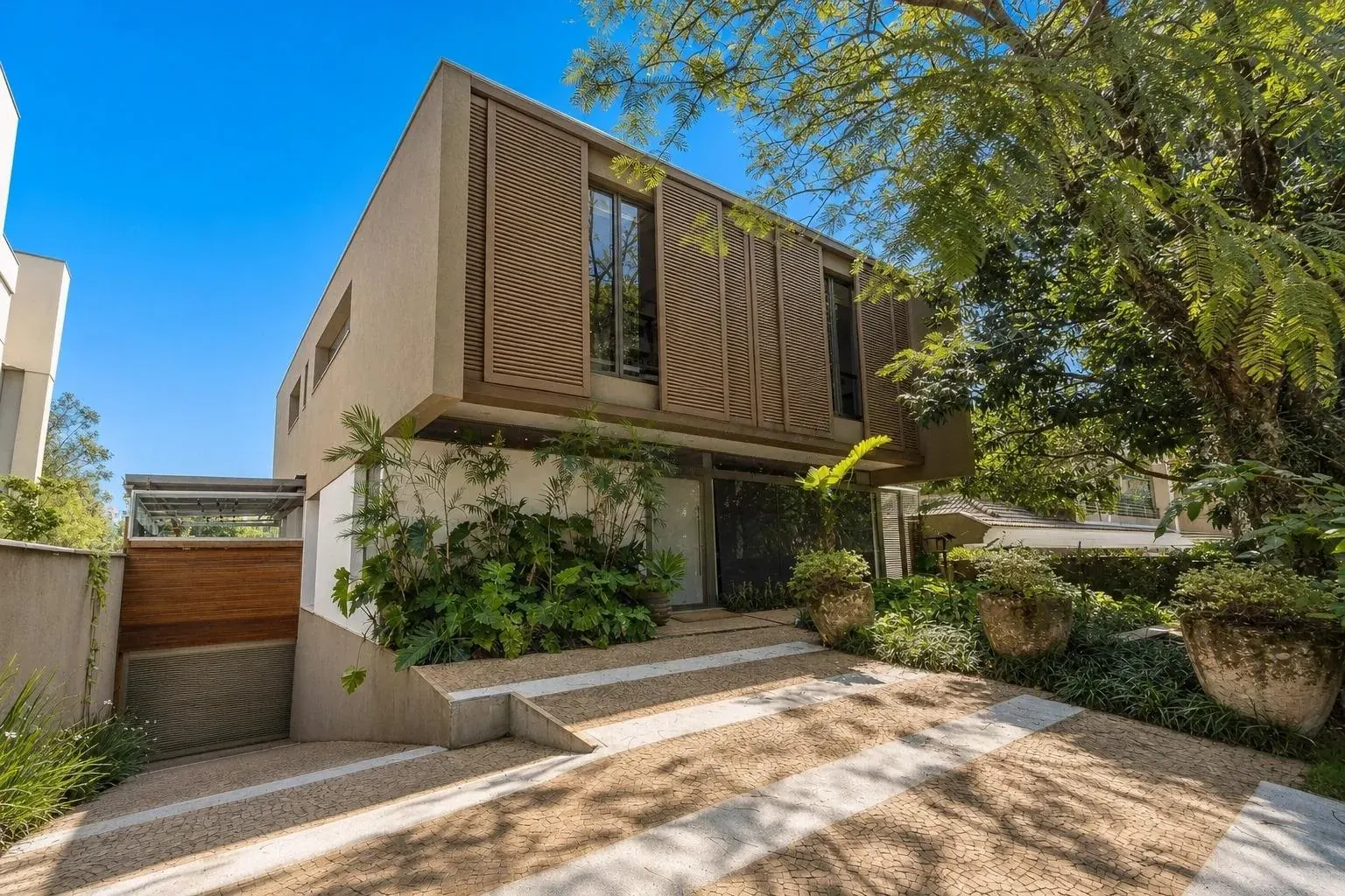 Fachada da casa com brises de madeira no pavimento superior e jardim de entrada