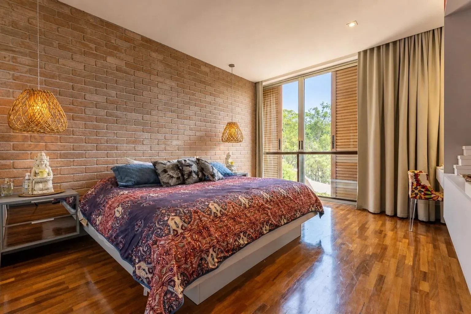 Suíte com parede de tijolo aparente, piso de madeira e cortinas do piso ao teto